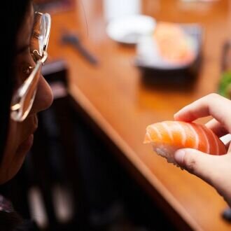 Woman eating nigiri sushi with salmon.