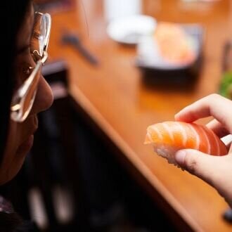 Woman eating nigiri sushi with salmon.