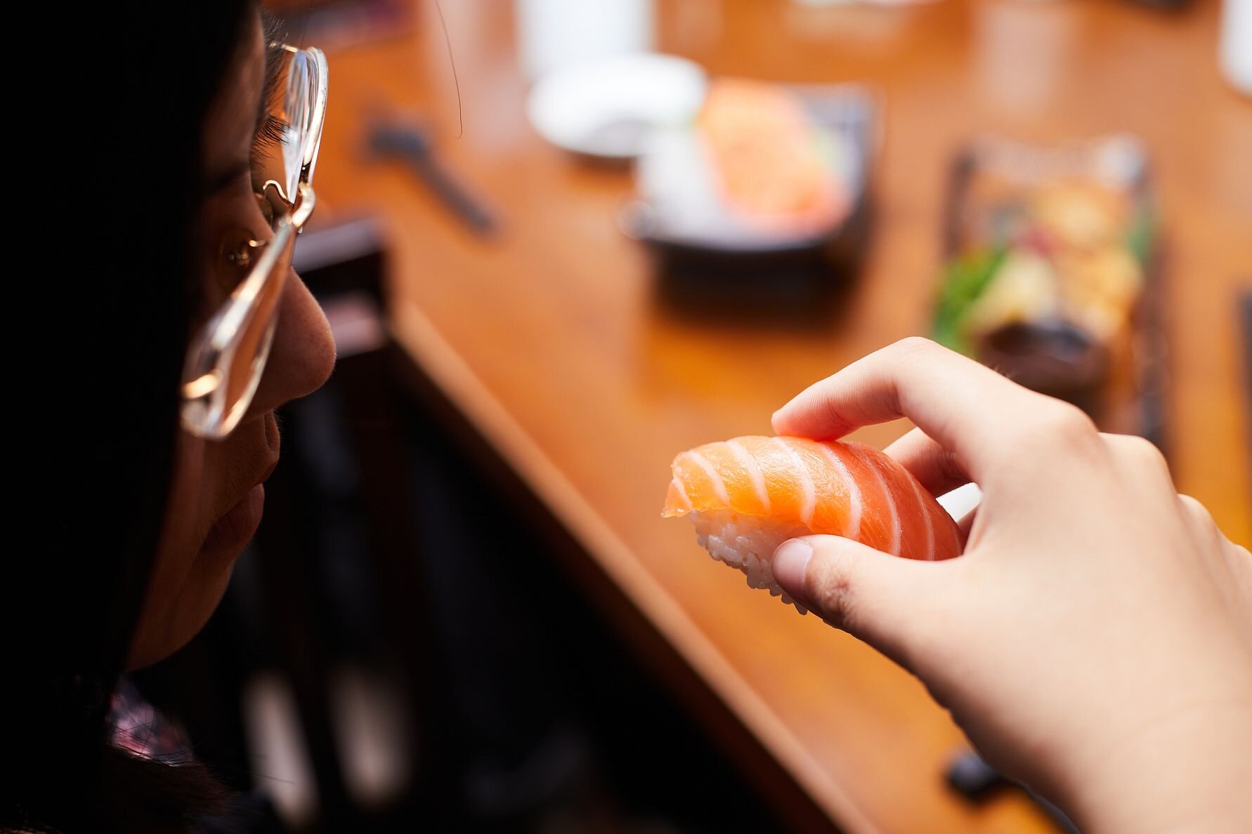 Woman eating nigiri sushi with salmon.
