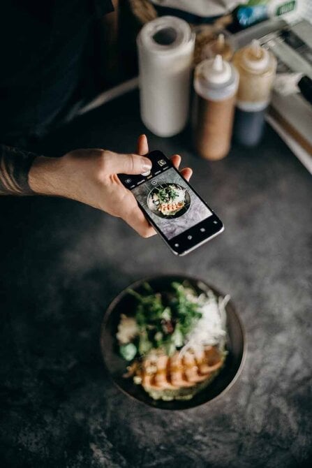 Hand and phone taking image of food on plate